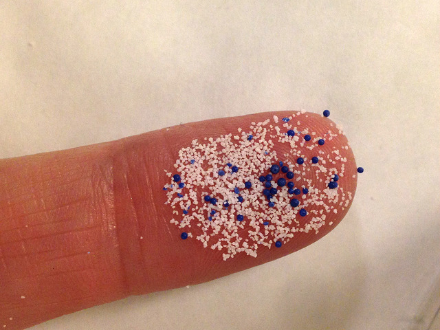 Plastic microbeads cling to a person's finger.