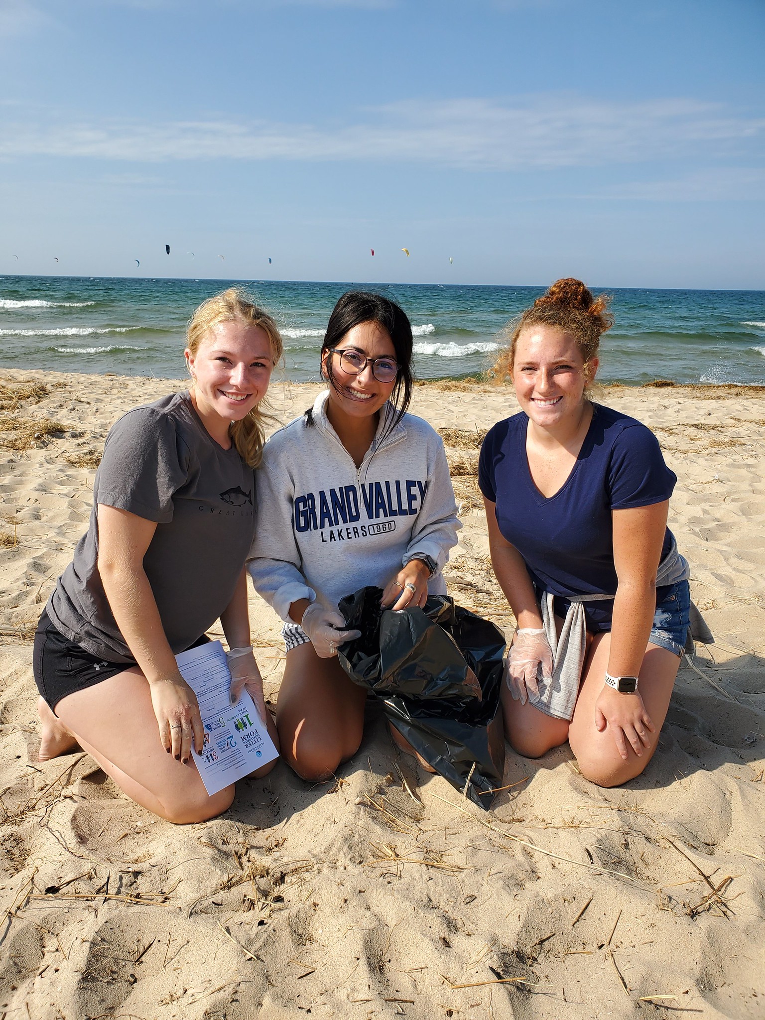 Three volunteers in sand in front of water