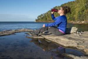 Women drinking from a water bottle on a Lake Superior shore, photo by Lloyd DeGrane