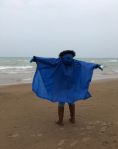 An Adopt-a-Beach volunteer in a poncho stands by Lake Michigan with arms outstretched.