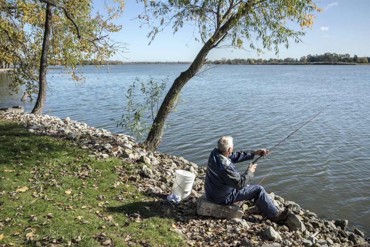 A man sits on the shoreline, fishing.