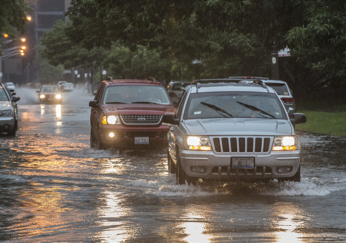 Cars drive through a flooded street.