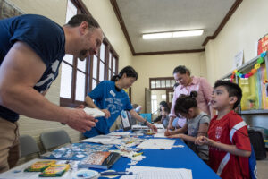 A man and woman interact with two children and their mother at a table covered with activities.