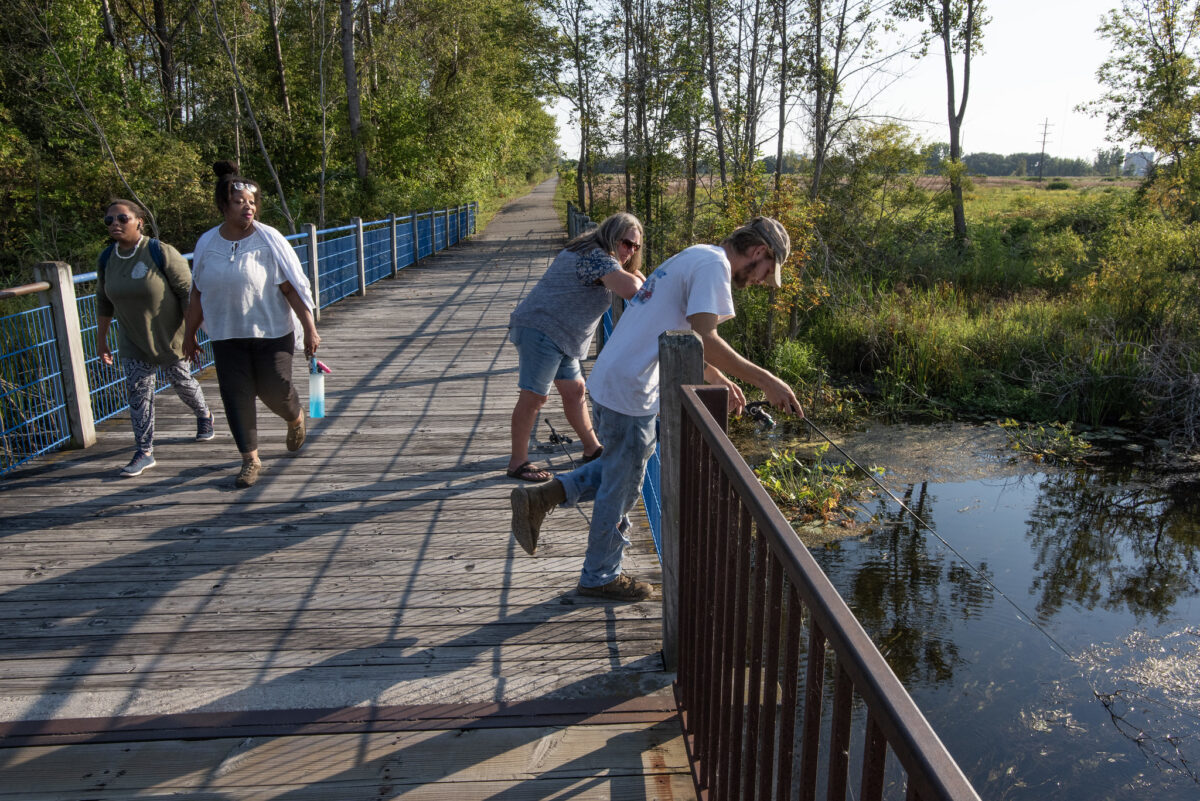 People fish and hike on a bridge by the water.