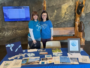 Two women stand behind a table filled with Great Lakes maps and papers.