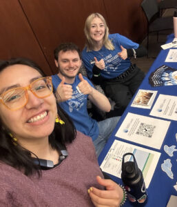 Three people behind a table full of Great Lakes materials smile at the camera.