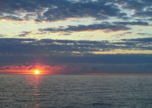 The sun rises in the horizon over a lake.