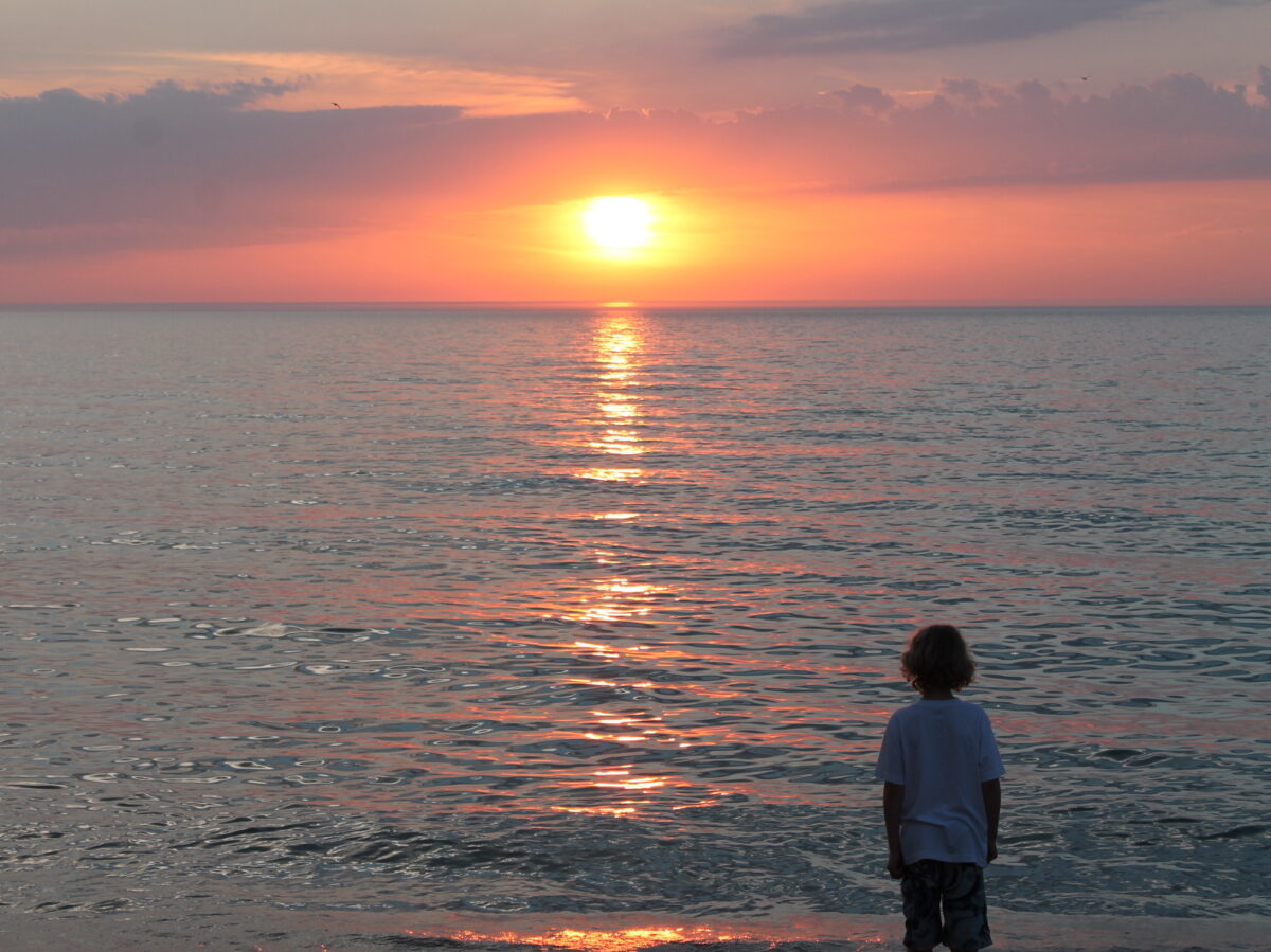 A boy looks out over the lake at sunrise.