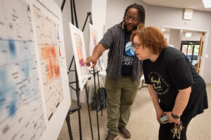 A man and a woman look at a map where some areas are marked in red.