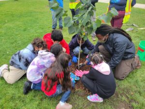 Six children and an adult plant a tree.